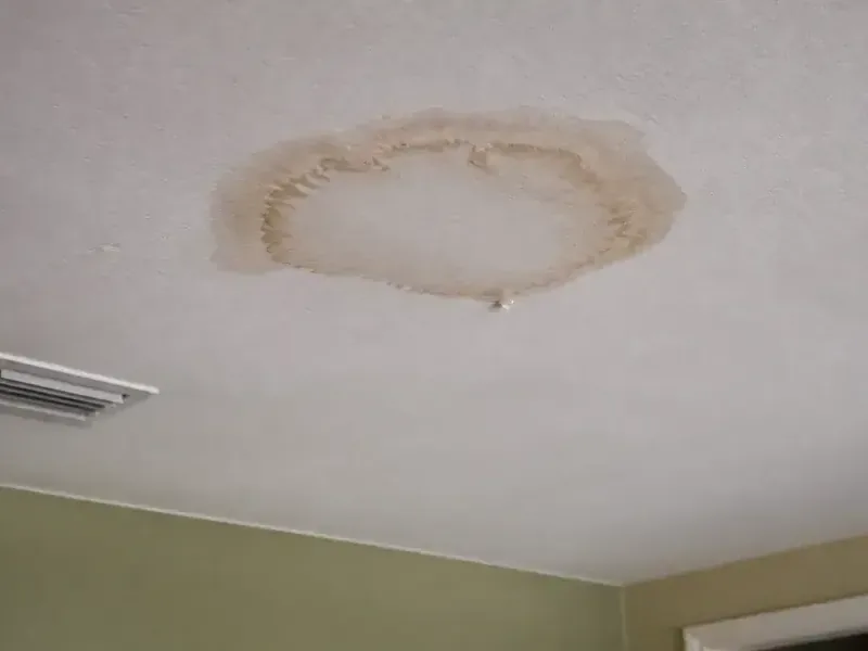 Circular water stain on a ceiling beside an air vent