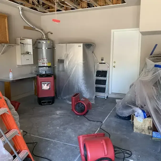 Red air movers and a dehumidifier drying a garage beneath an opened ceiling