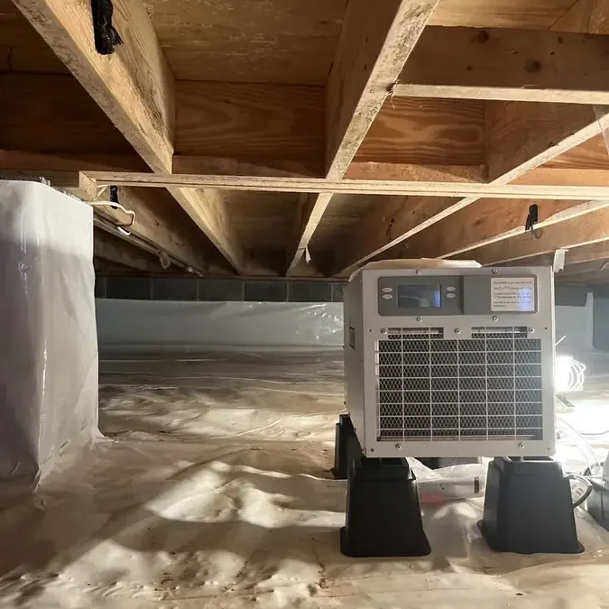 A dehumidifier beneath exposed wooden joists in a crawl space