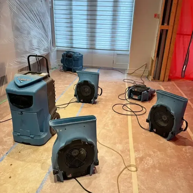 Air movers and a dehumidifier surround an exposed wood floor